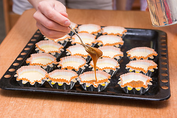 Image showing Boiled condensed milk added to raw cupcakes workpiece lying on a baking sheet