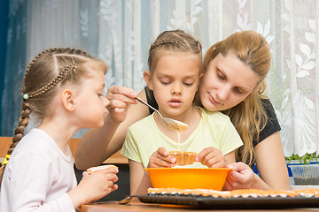 Image showing Mother and two children baking pour the mass into molds preparing muffins for Easter