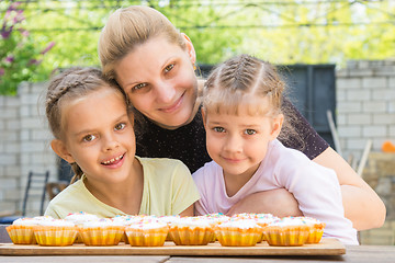 Image showing Mother hugging her daughters who cook delicious cupcakes