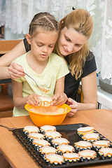 Image showing Mother helps daughter to pour batter into the mold for cupcakes