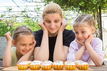 Image showing Mother and two daughters with a good appetite and big eyes looking at easter cupcakes