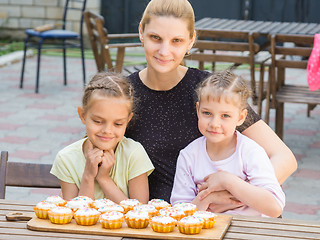 Image showing Mom and two daughters sitting at a table on which lay cooked them Easter cupcakes