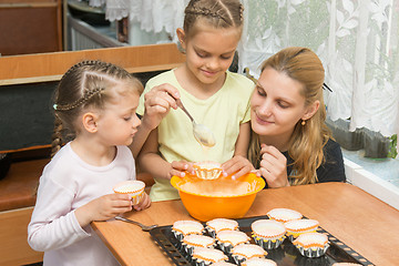 Image showing The elder daughter pours batter for cakes in tins, under the care of my mother and younger sister