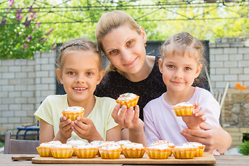 Image showing Mother and two daughters sitting at the table with Easter cupcakes in his hands and looked into the frame