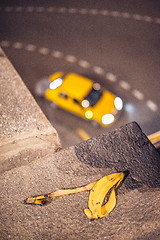 Image showing yellow taxi cab passing corner on the blurred background with banana skin in front