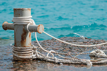 Image showing Rusty mooring bollard with ship ropes and  clear turquouse sea ocen water on background