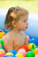 Image showing The little baby girl playing with toys in inflatable pool in the summer sunny day