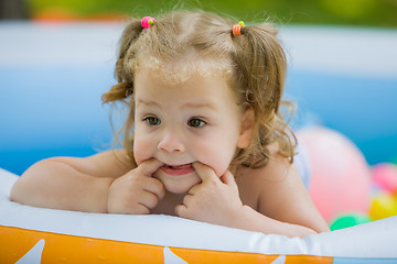 Image showing The little baby girl playing with toys in inflatable pool in the summer sunny day