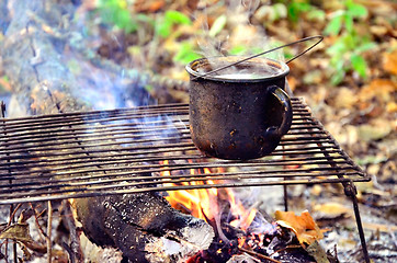 Image showing Tourist fire with a mug of boiling water on Camping