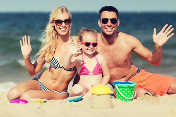 Image showing happy family with sand toys waving hands on beach