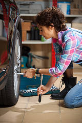 Image showing woman mechanic in overalls tighten the fixing bolts on the wheel