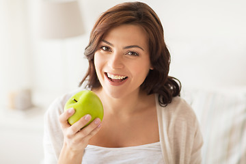 Image showing smiling young woman eating green apple at home