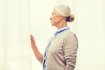 Image showing lonely senior woman looking through window at home