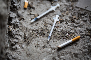 Image showing close up of syringe and smoked cigarette on ground