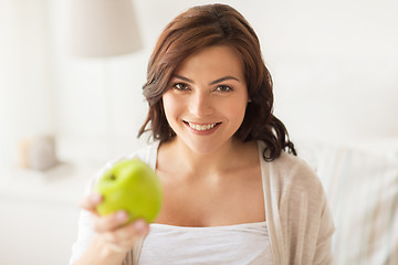 Image showing smiling young woman eating green apple at home