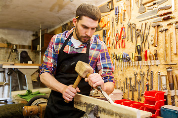 Image showing carpenter with wood, hammer and chisel at workshop