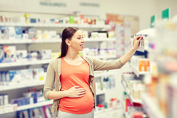 Image showing happy pregnant woman choosing medicine at pharmacy