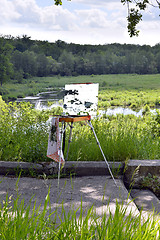 Image showing Hands of the artist with a brush, paint a picture on an easel in the open air