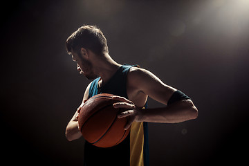 Image showing Silhouette view of a basketball player holding basket ball on black background