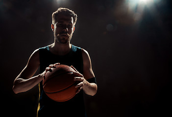 Image showing Silhouette view of a basketball player holding basket ball on black background