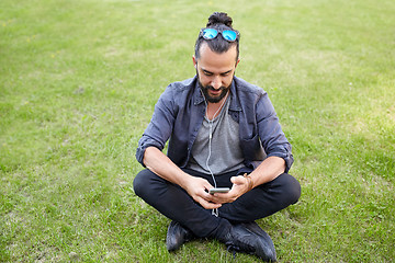 Image showing man with earphones and smartphone sitting on grass