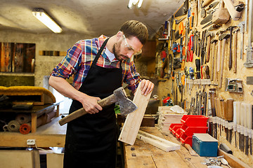 Image showing carpenter with ax and board working at workshop