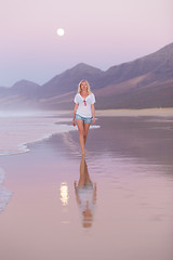 Image showing Lady walking on sandy beach in sunset.