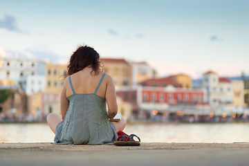 Image showing Rear view of woman sitting on a pier, reading book.