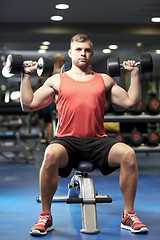 Image showing young man with dumbbells flexing muscles in gym