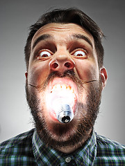 Image showing Caucasian man with bulb in his mouth on gray background