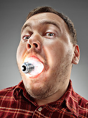 Image showing Caucasian man with bulb in his mouth on gray background