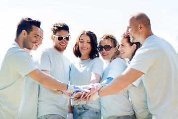 Image showing group of volunteers putting hands on top in park