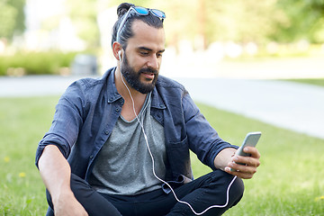 Image showing man with earphones and smartphone sitting on grass