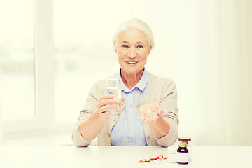 Image showing happy senior woman with water and medicine at home