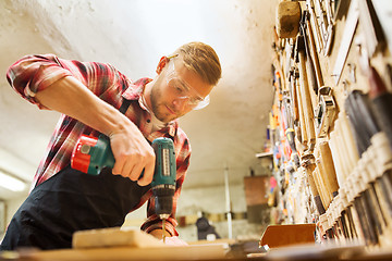 Image showing carpenter with drill drilling plank at workshop