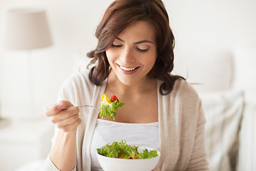 Image showing smiling young woman eating salad at home