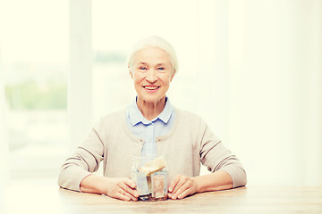 Image showing senior woman with money in glass jar at home