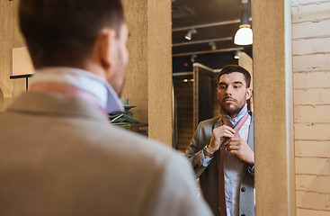 Image showing man tying tie on at mirror in clothing store