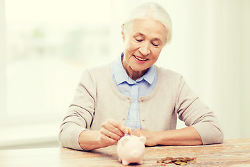 Image showing senior woman putting money to piggy bank at home