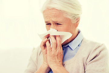 Image showing sick senior woman blowing nose to paper napkin