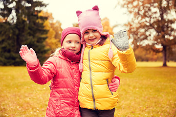 Image showing two happy little girls waving hand in autumn park