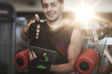 Image showing young man with tablet pc showing thumbs up in gym