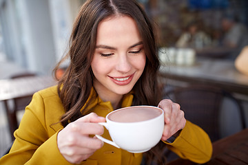 Image showing happy woman drinking cocoa at city street cafe