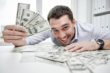 Image showing happy businessman with heap of money in office