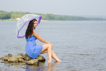 Image showing Lonely sad young woman with an umbrella sits on a rock by the river