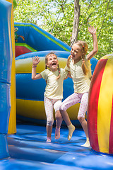 Image showing Two girls grimacing happily jumping on an inflatable trampoline