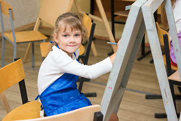 Image showing Girl draws pencil on an easel to draw a lesson and looked into the frame