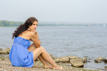 Image showing Lonely sad young girl sitting on the river bank