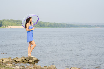 Image showing Lonely sad young girl with an umbrella stands on the bank of the river and looks into the distance