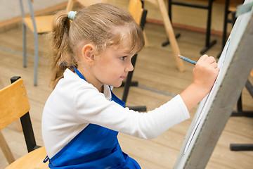 Image showing Five-year girl paints on an easel in the drawing lesson